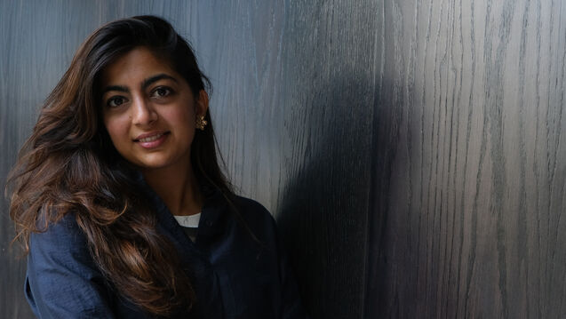 Sneha standing in front of a black wood wall, smiling at the camera.