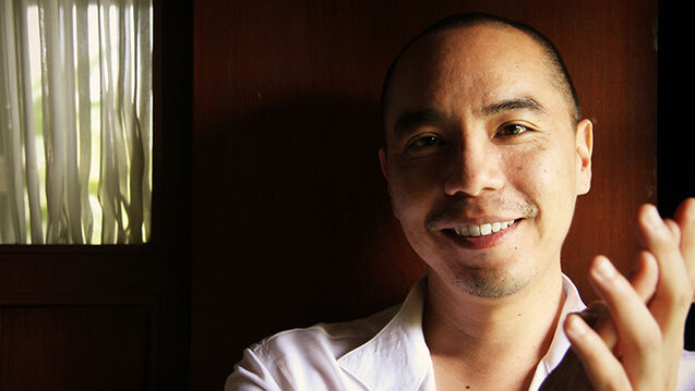 A headshot of Apichatpong Weerasethakul  in front of a brightly lit curtain.