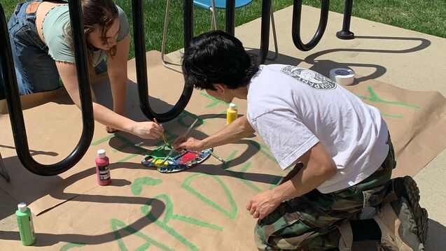  Two students painting a sign on the sidewalk by a bike rack