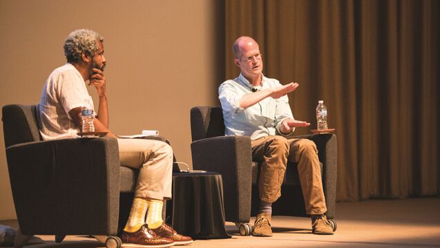 Two people seated in discussion on a stage.