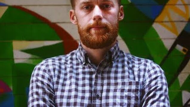 Charles Corwin stands with his arms crossed over his chest. He wears a checkered shirt.