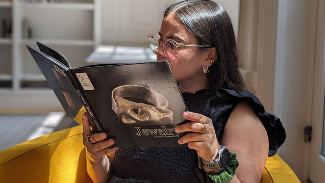 A young woman stands in front of an ornate mirror and fireplace