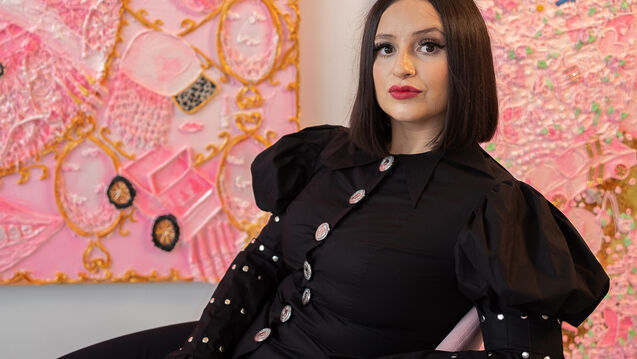 An artist poses in front of a pink canvas