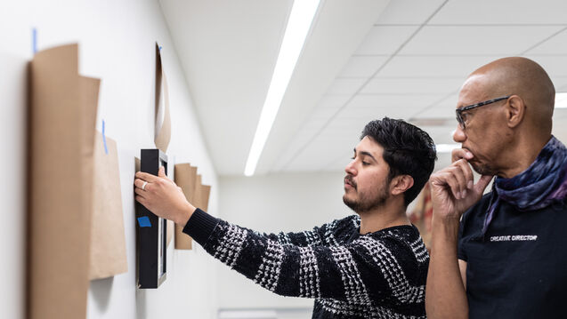 Two people collaborating on hanging an art piece