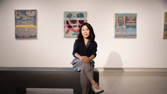A photo of SAIC president Jiseon Lee Isbara sitting down in front of three works of art.