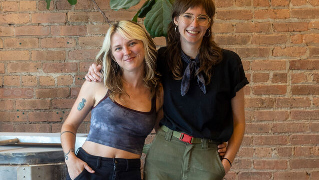 Two artists stand in front of a brick wall
