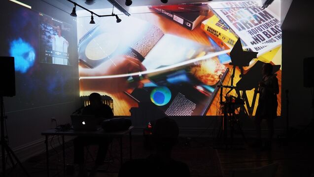 Still of a performance piece by Fleming and Hunter Whittaker-Morrow that includes colorful projections in a dark room