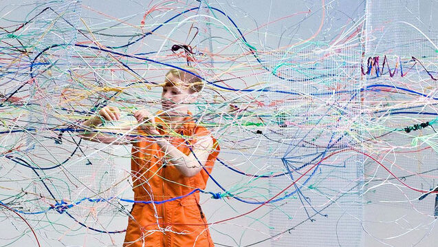 An artist stands amidst static, colored wires
