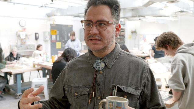 A faculty member talks to the camera in front of a ceramics class
