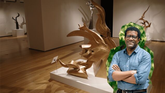 Portrait of Ross Stanton Jordan with glasses, wearing a blue button-up shirt and standing with arms crossed, digitally placed in front of a museum gallery of abstract bronze sculptures on wooden floors.