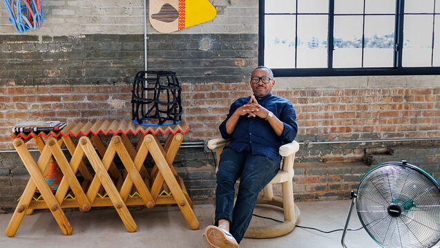 Portrait of Norman Teague, an adult Black person with a medium-dark skin tone, seated in his studio space.. 