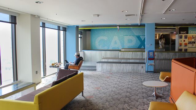 A student sits with headphones on looking at a laptop facing a window.