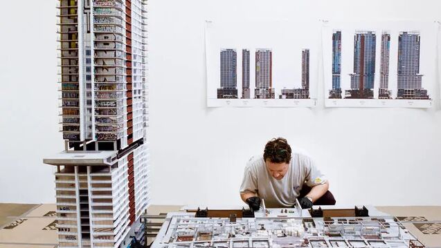 Gomez working on his nine-foot sculpture, adding details with pins, glue and small cutouts of paper. A fabrication team built the basic structure, then affixed 3-D printed details. Gomez weathered the towers with paint and varnish and added the graffiti miniaturizations.