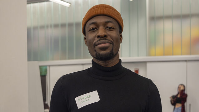 Headshot of a person with a medium-dark skin tone holding a laptop and wearing a nametag that reads "UTHMAN Olowa."