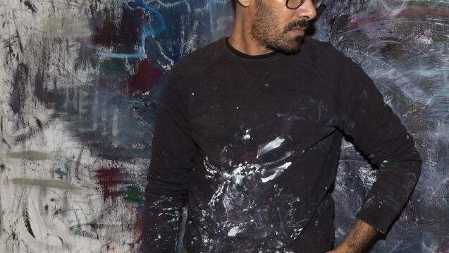 Artist Abdulrahman Hamdi stands in front of an abstract painting