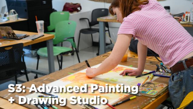 A student leans over a table where they are painting.
