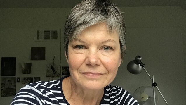 CAPX Director Kate Schutta, a person with light skin tone and short gray hair, seated at a desk in a bright office.