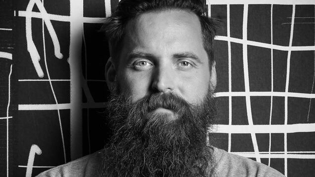 A black and white photo of an artist with a beard