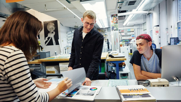 Three students of varying skintones and genders gathered around a counter. 