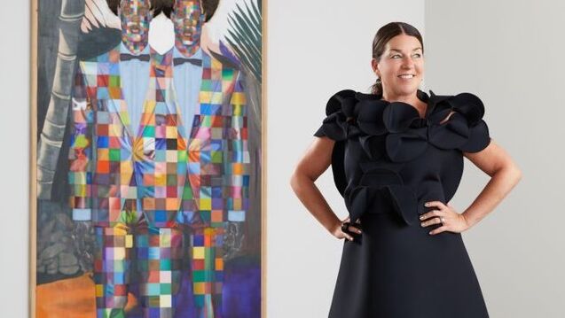 A curator in a black dress poses in front of a colorful canvas