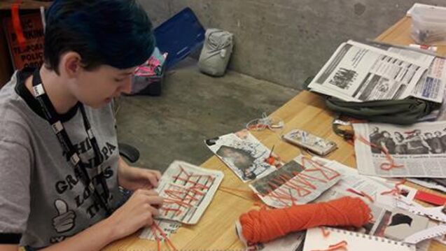 Writing student using yarn to thread words through newspaper.