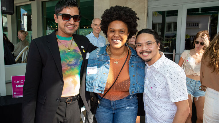 Three smiling people pose for the camera at a sunny outdoor event