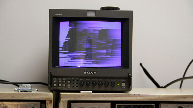 A small, vintage tv sitting on top of a sound board. An abstract video with purple shapes is playing.