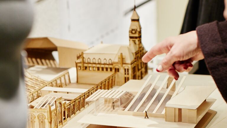 A person points at details of a wooden laser cut architectural model.