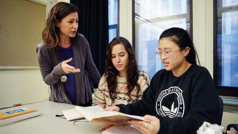 Professor explaining concepts to two students in a classroom