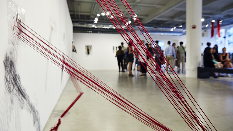 Art installation featuring red strings affixed to a gallery wall.