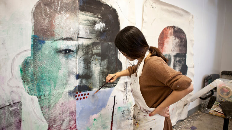 A person painting on a large canvas in a studio. 