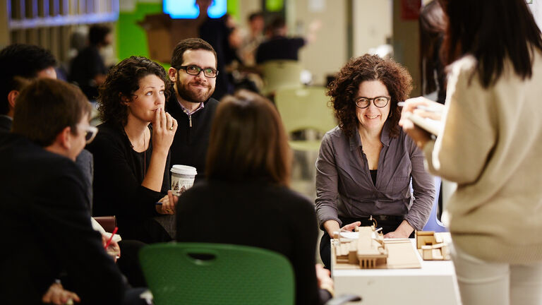 A group of people sitting and talking in front of an architectural model.