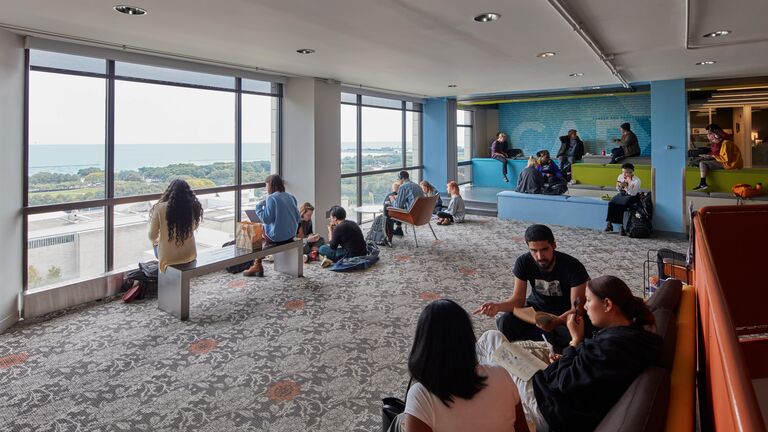 Students talking with each other and studying in a large lounge space on the fourteenth floor of an SAIC campus building overlooking Grant Park and Lake Michigan.