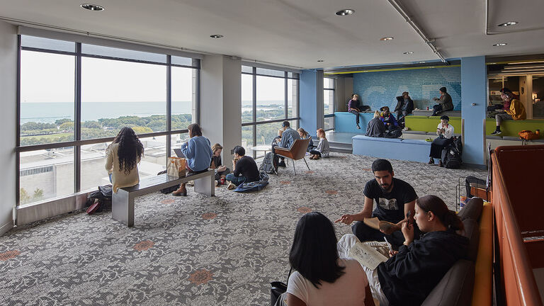 Students gathered around a lounge talking, studying, and gazing out the windows at the view overlooking the Art Institute museum.