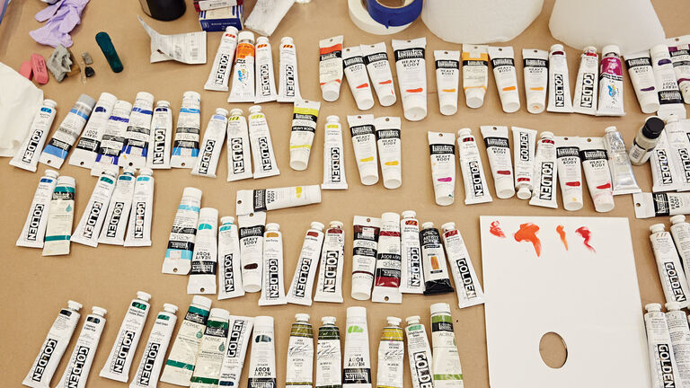 Various tubes of paints lined up alongside other painting materials such as tape, water, brushes, and palettes.