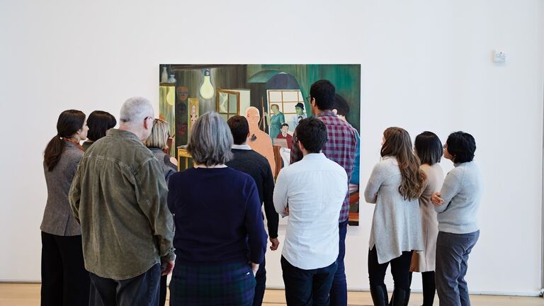 A group of students gathers before a painting in a museum gallery