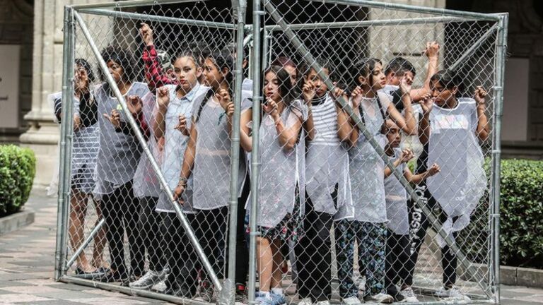 A group of young people imprisoned in a small chain-link box