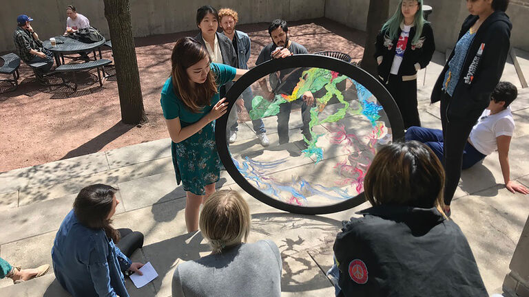 A group of students observing a professor using a large circular, glass object. 