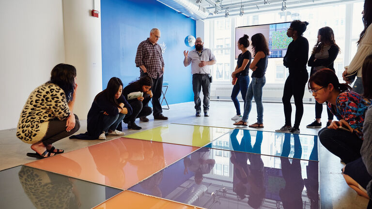 An image of some students observing a large piece of art on the floor in the School of the Art Institute of Chicago's gallery space. 