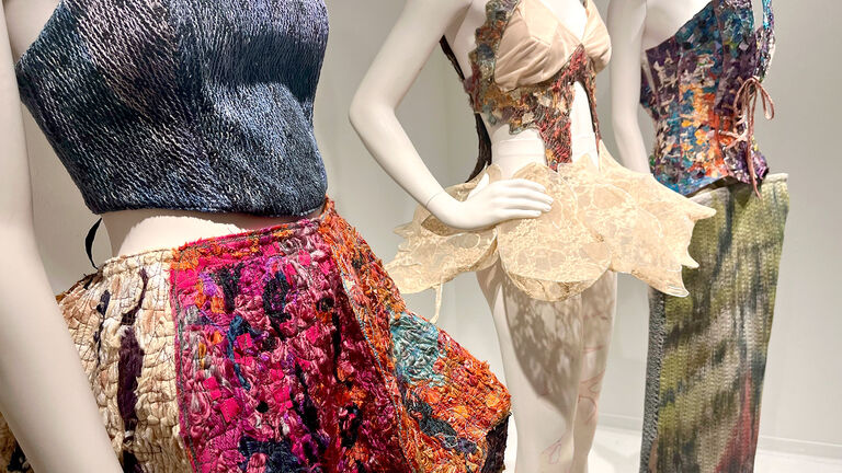 Three mannequins wearing colorful, elaborate outfits.