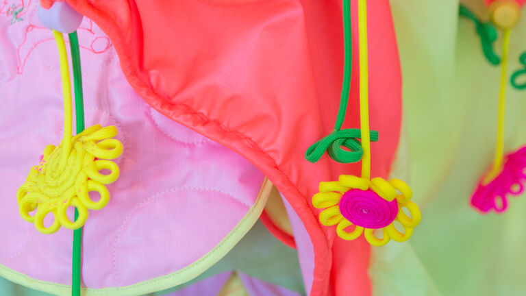 An image of brightly pink, green and yellow fluorescent fabric with flower details. 