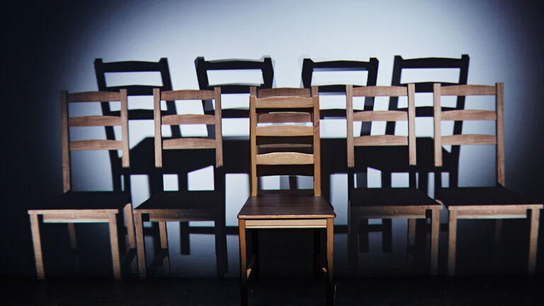 An image of several wooden chairs with a bright light creating shadows accross the walls. 
