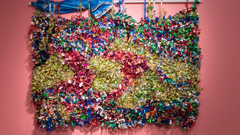 Multi-colored bows covering a large panel hanging on a pink wall using a beach umbrella. 