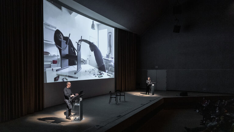 Two people standing on a large stage with a projection behind them. 