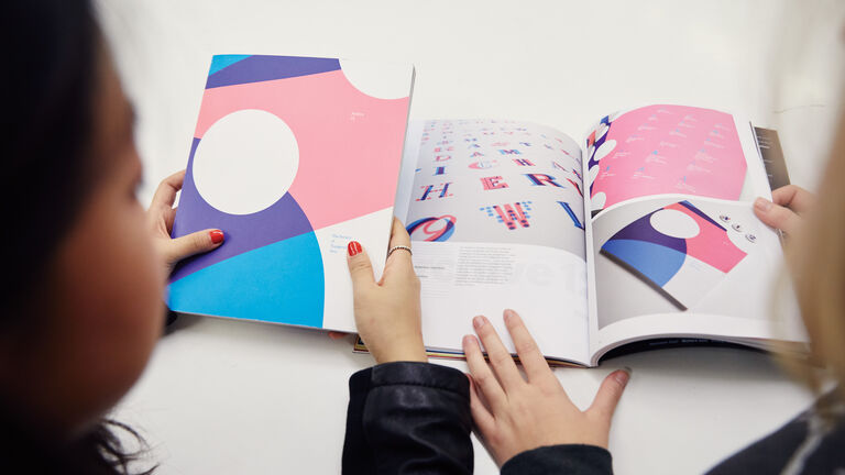 Two people looking at a purple, pink and blue booklet. 