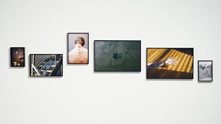 Multiple photographs in various sizes hanging in on a white, gallery wall. 