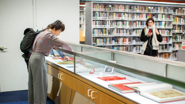 Two people looking at books in a glass case inside a library. 