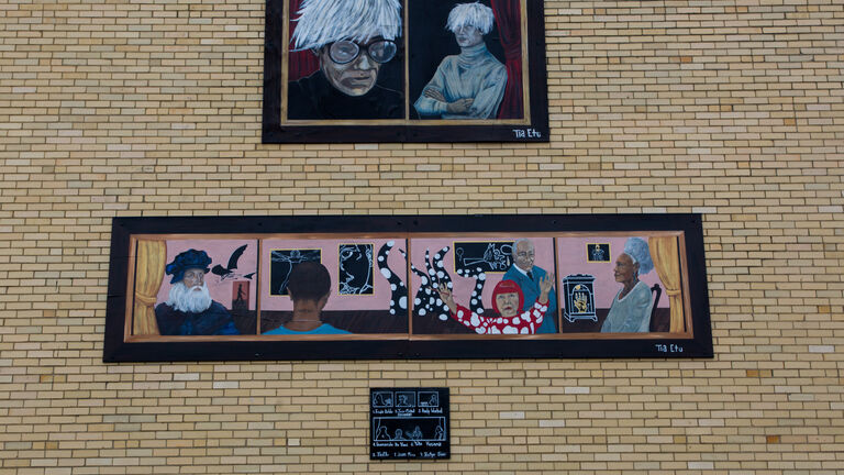 A series of paintings on a brick wall depicting many famous artists 