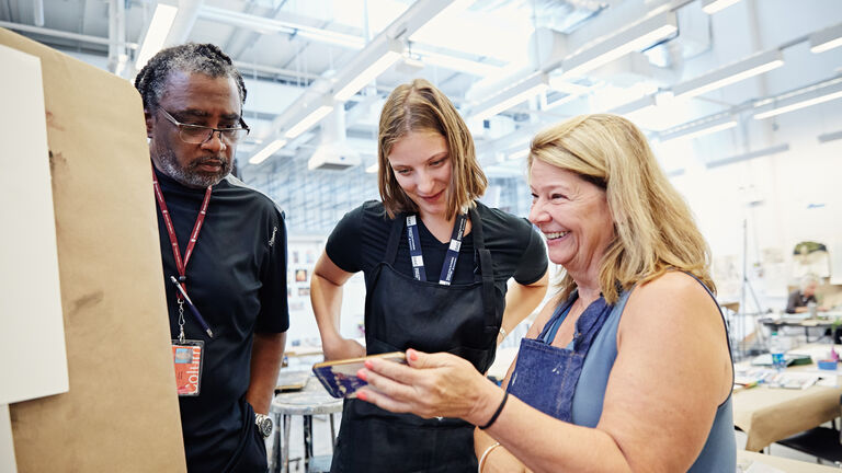 A student shows two teachers an image on her phone in an art classroom