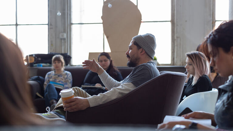 Graduate students sitting together in a large room engaged in discussion with one another.